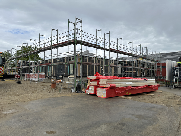 Auf der Baustelle steht ein teilweise eingerüstetes Gebäude, umgeben von Baumaterialien und Baugeräten.