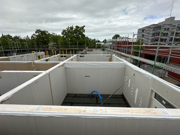Eine Baustelle mit noch nicht fertiggestellten Gebäudeteilen aus weißen Wänden, umgeben von Gerüsten und in der Nähe von anderen modernen Gebäuden.