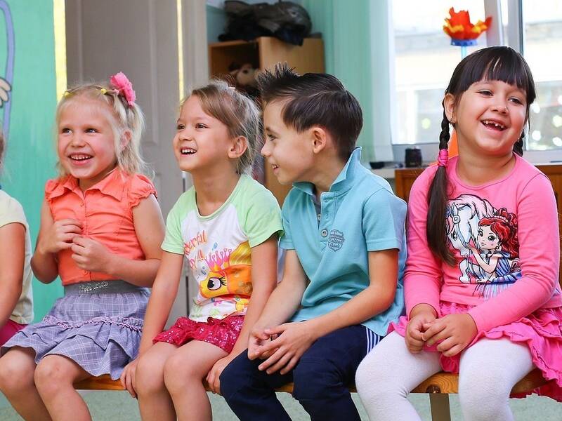 Eine Gruppe von fröhlichen Kindern sitzt nebeneinander auf einer Bank in einem bunt dekorierten Raum