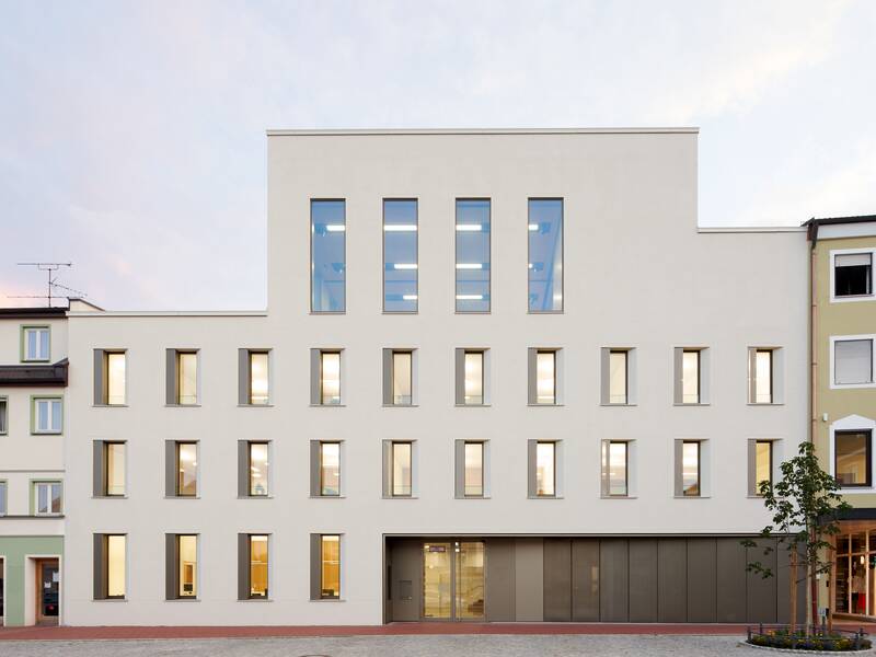 Das Bild zeigt das Rathaus der Stadt Dorfen, ein modernes, mehrstöckiges Gebäude mit einer schlichten Fassade und zahlreichen Fenstern, flankiert von traditionellen Gebäuden.