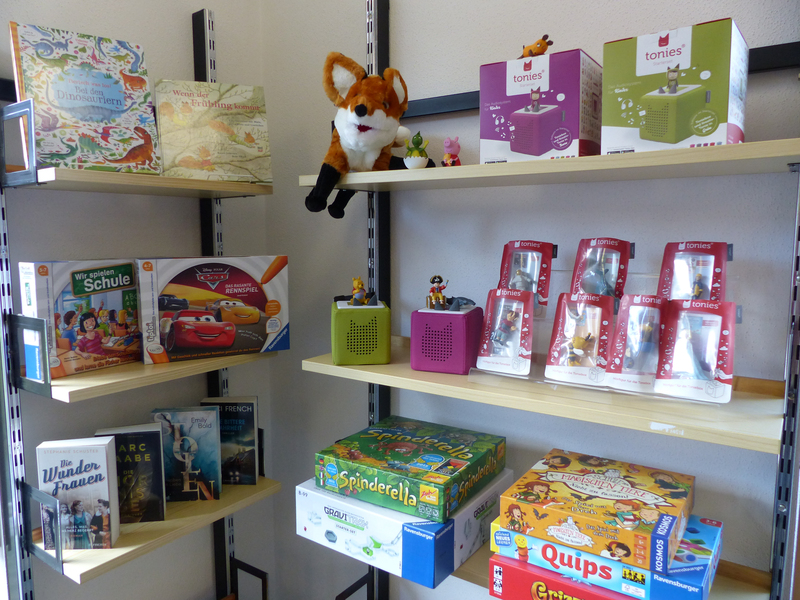 Ein Regal gefüllt mit verschiedenen Kinderspielen, Spielzeugfiguren und Büchern, darunter Boxen mit Tonies und ein Plüschfuchs.