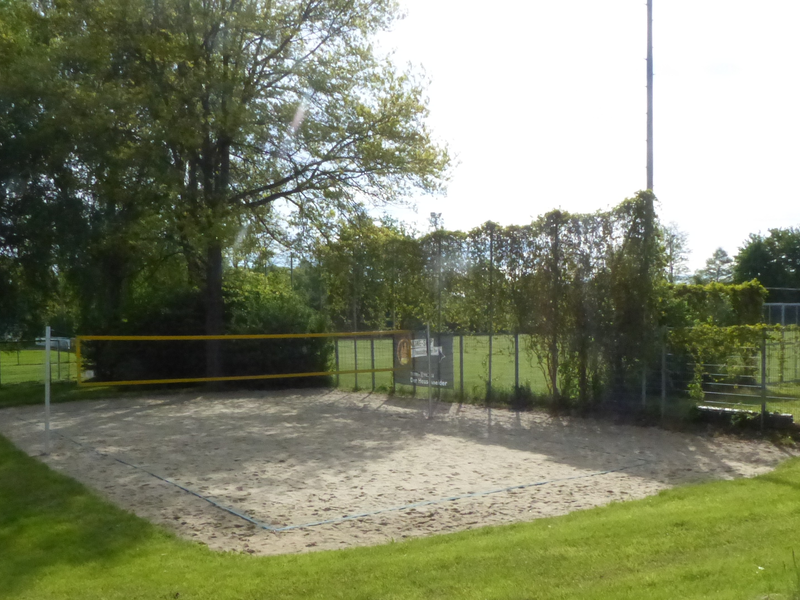 Beachvolleyballplatz umgeben von grünem Rasen und Bäumen.