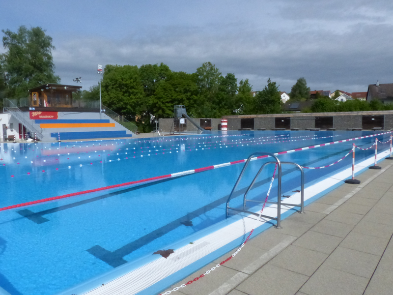 Schwimmbecken mit Schwimmbahnen. Im Hintergrund eine Tribüne.