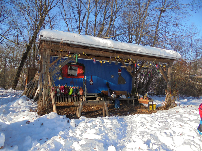 Eine blau gestrichene Hütte mit festlichen Dekorationen und Kinderschuhen unter einem Dach im verschneiten Wald.