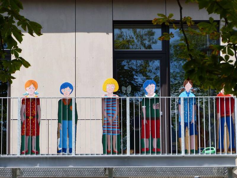 Sechs Pappbilder von Kindern, die ganz unterschiedlich aussehen, stehen auf einem Balkon.