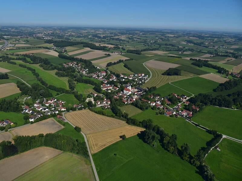Das Bild zeigt eine ländliche Landschaft mit Feldern, Wäldern mit der Ortschaft Schwindkirchen in der Mitte, durch die eine Staatsstraße führt.