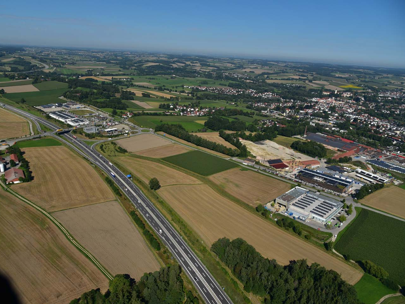 Die A94 führt durch eine weitläufige ländliche Landschaft mit Feldern und vereinzelten Gebäuden. Dahinter ist die Stadt Dorfen mit dem Gemeindegebiet Hausmehring zu sehen.