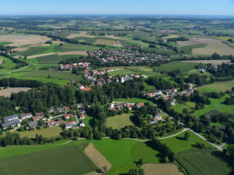 Eine luftige Landschaftsaufnahme zeigt eine kleine Ortschaft, umgeben von grünen Wiesen und Feldern.