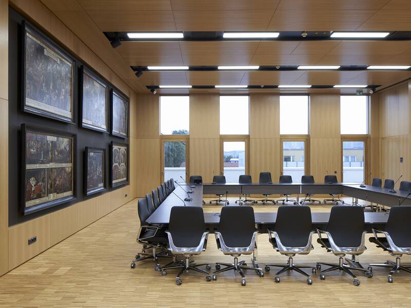 Ein moderner Konferenzraum mit einem großen, ovalen Tisch, umgeben von schwarzen Bürostühlen, Holzwänden, und mehreren Gemälden an der linken Wand.
