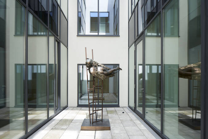 In einem modernen Innenhof mit Glaswänden steht eine abstrakte Skulptur auf einer Metallstruktur.