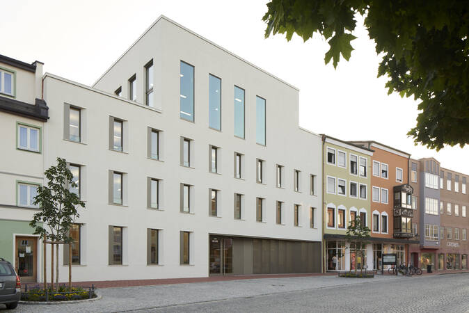Eine Straßenansicht mit modernen und traditionellen Gebäuden, darunter das Rathaus, ein großes, schlichtes, weißes Gebäude mit großen Fenstern.