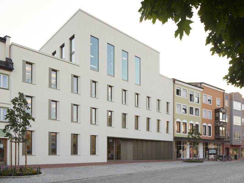 Eine Straßenansicht mit modernen und traditionellen Gebäuden, darunter das Rathaus, ein großes, schlichtes, weißes Gebäude mit großen Fenstern.