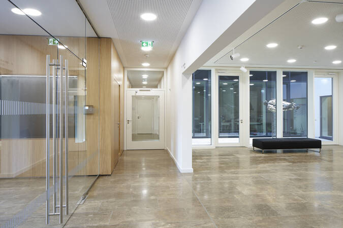 Helle und geräumige moderne Eingangshalle mit Glastüren, einem schwarzen Sitzbank und hellen Fliesenboden.