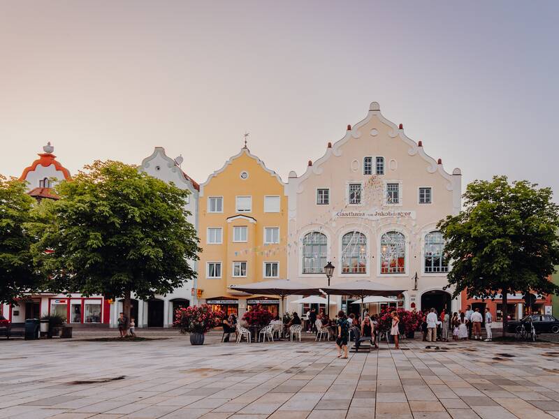 Eine Reihe bunter Giebelhäuser in einer Stadt, darunter ein großes Gebäude mit der Aufschrift "Gasthaus zum Jakobmayer".