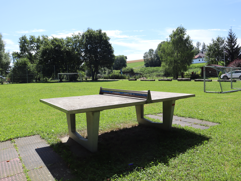 Im Vordergrund steht eine Tischtennisplatte. Dahinter ist ein Bolzplatz mit zwei Fußballtoren.