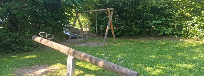 Spielplatz in Eibach mit Schaukel, Rutsche und Wippe umgeben von Bäumen und Büschen für viel Schatten