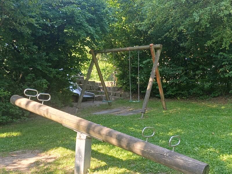 Spielplatz in Eibach mit Schaukel, Rutsche und Wippe umgeben von Bäumen und Büschen für viel Schatten