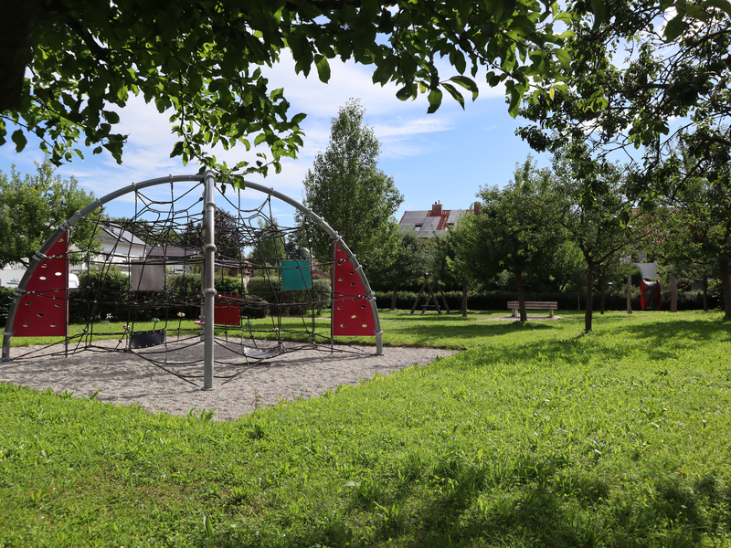 Ein Spielplatz von Bäumen umgeben. In der Mitte ein großes Klettergerüst.