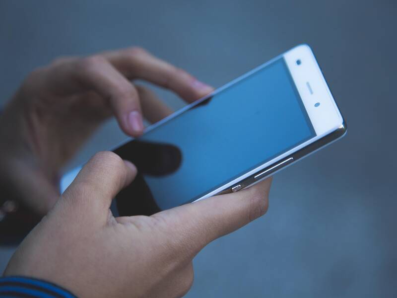 Eine Person hält ein Smartphone in beiden Händen und bedient es.