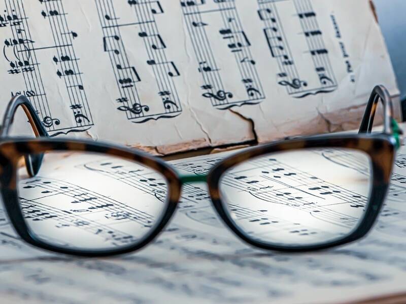Eine Lesebrille liegt auf geöffneten Notenblättern, wobei die Noten durch die Brillengläser klar fokussiert sind.