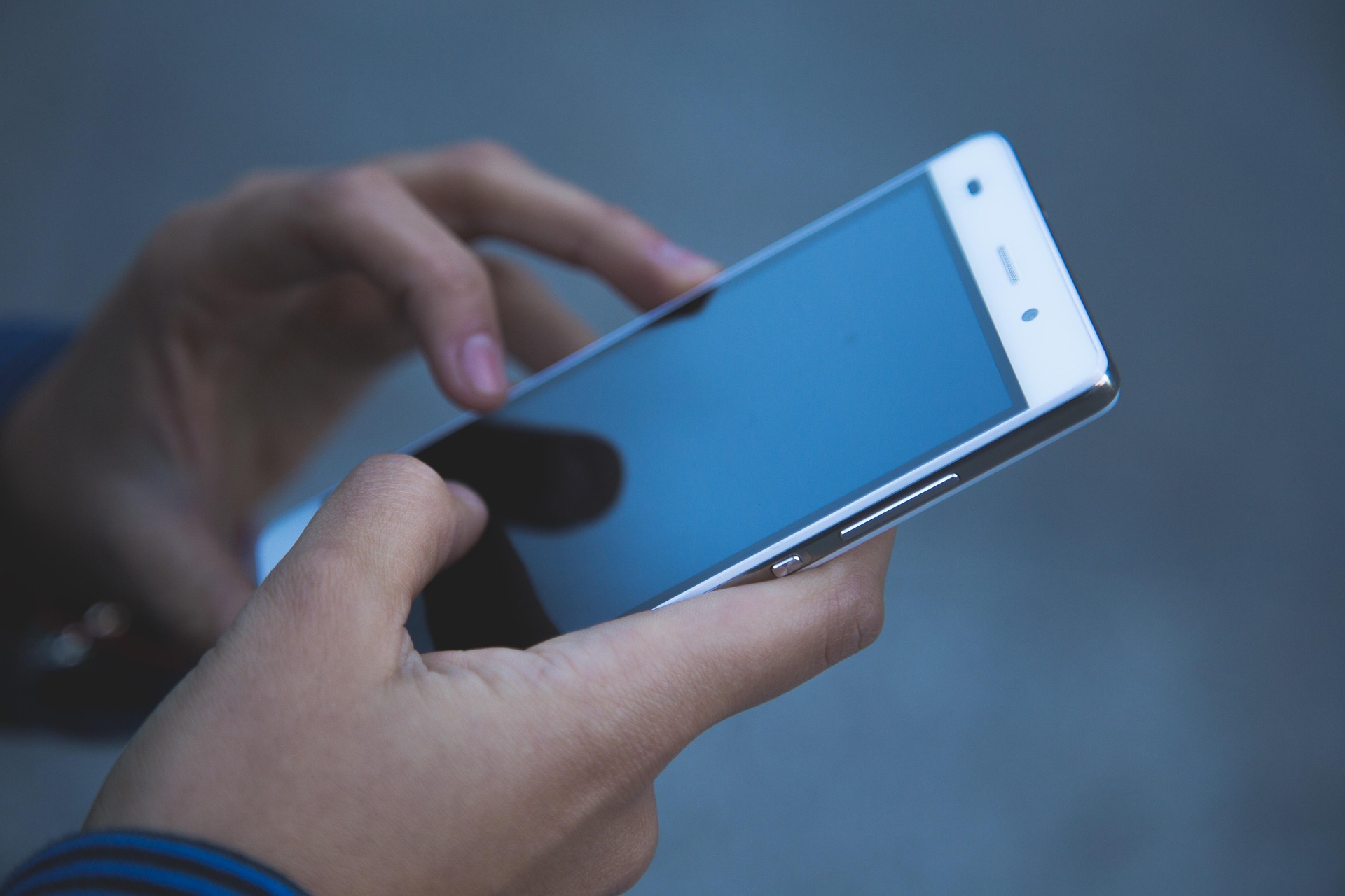 Eine Person hält ein Smartphone in beiden Händen und bedient es.